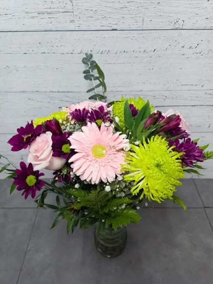 Bouquet de fleurs colorées dans un vase, comprenant des gerberas, des roses roses, des marguerites et d'autres fleurs.